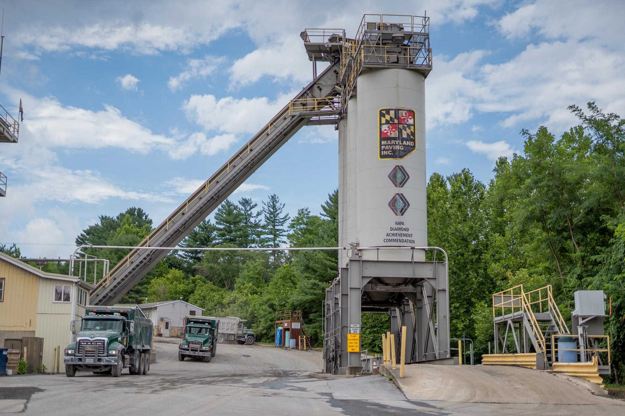 Large asphalt storage silos at a paving plant located in maryland, green trucks parked below, owned and operated by Gray & Son a leading site and development contractor in Maryland.