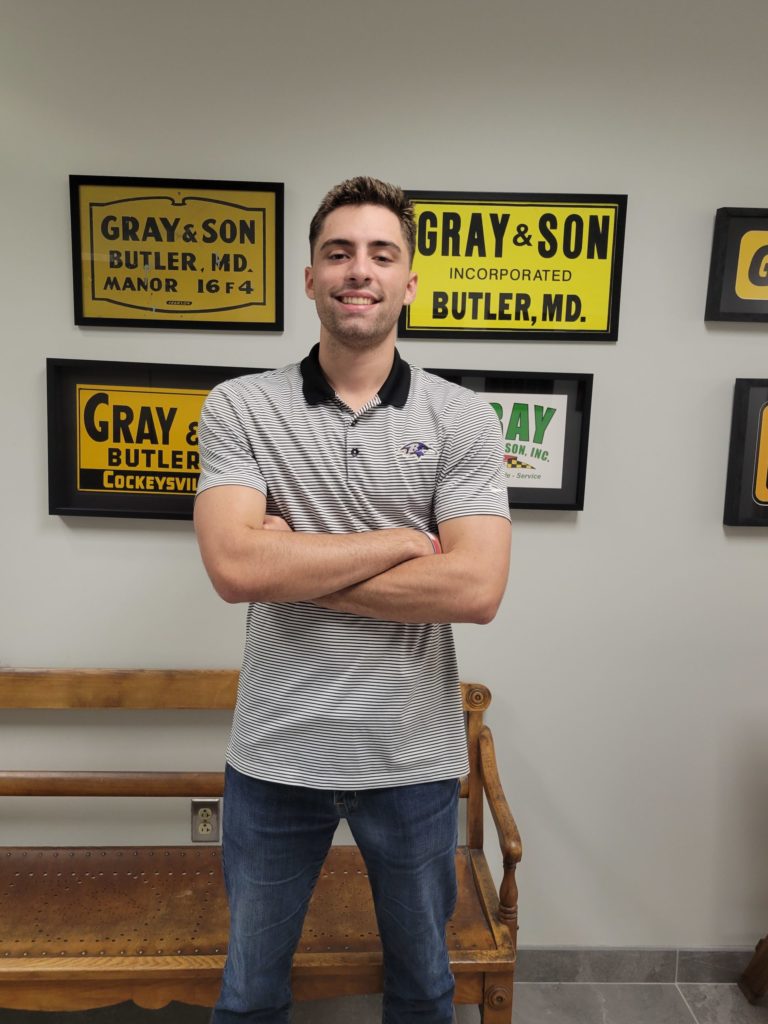 A full length photo of a man standing and smiling at the camera in an office who works for a company named Gray & Son a leading site and development contractor in Maryland.