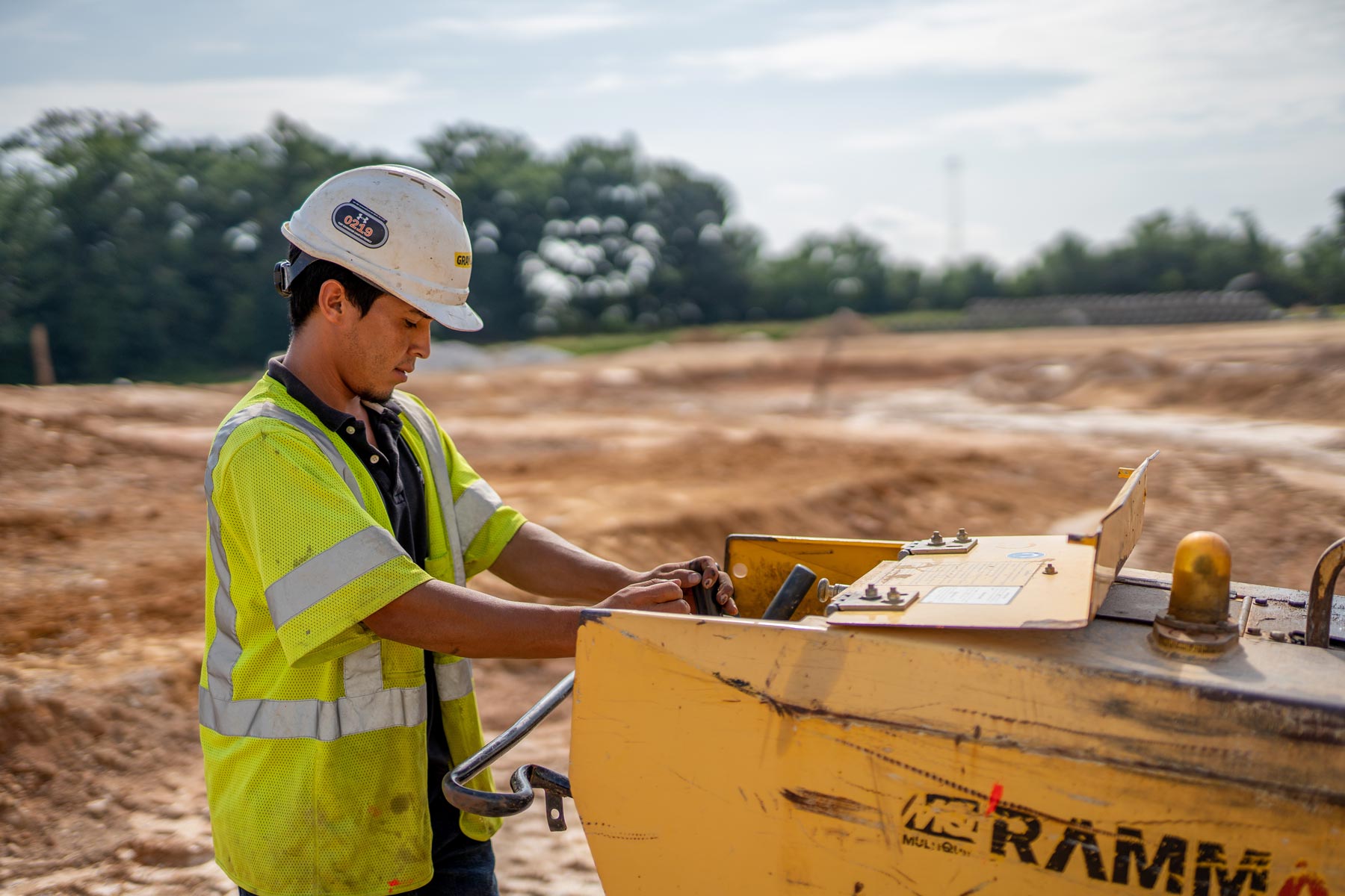 a male construction worker, in a dirt field controlling a machine who works for Gray & Son a leading site and development contractor in Maryland.