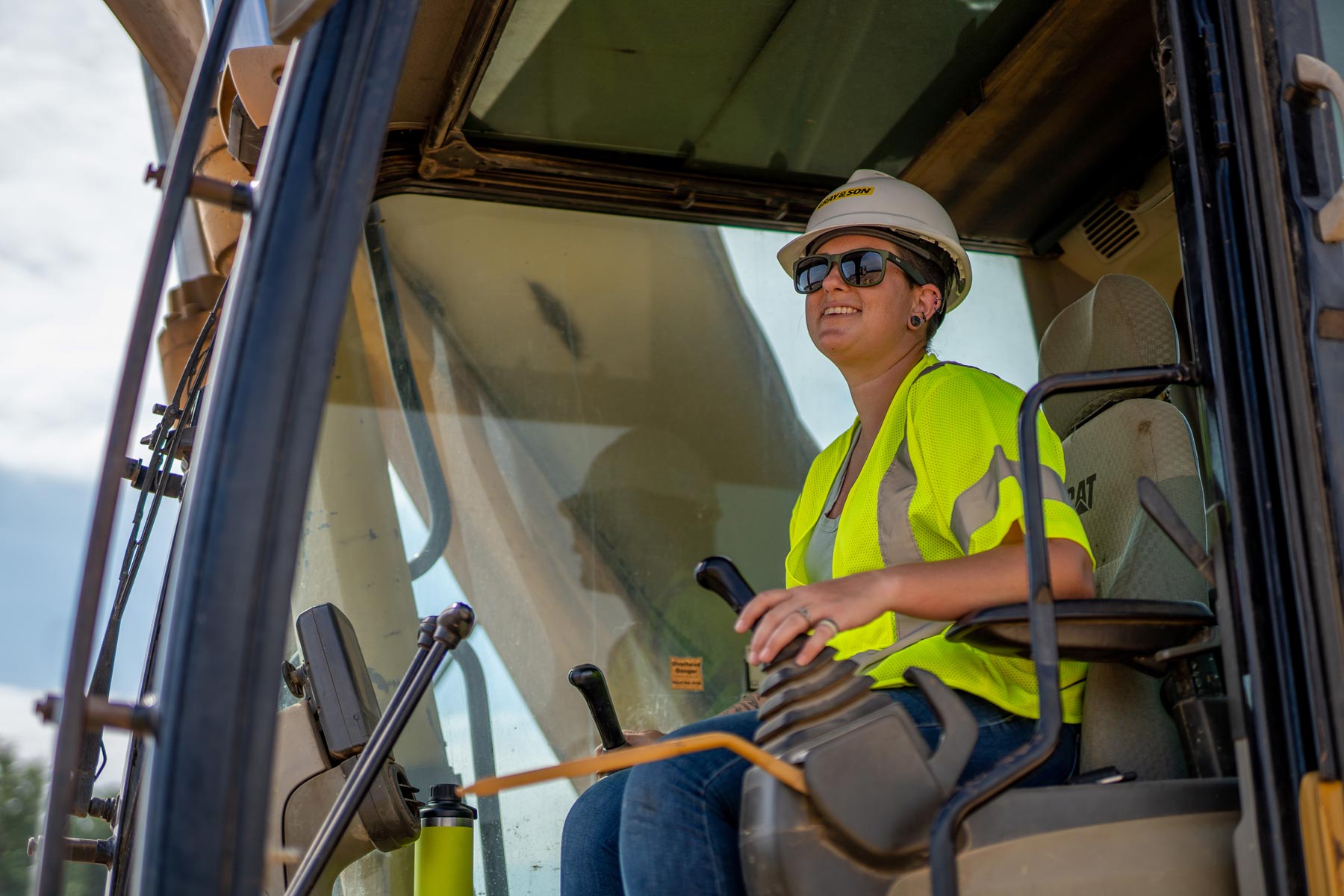 a female construction worker smiling while sitting and operating a large crane working for Gray & Son a leading site and development contractor in Maryland.