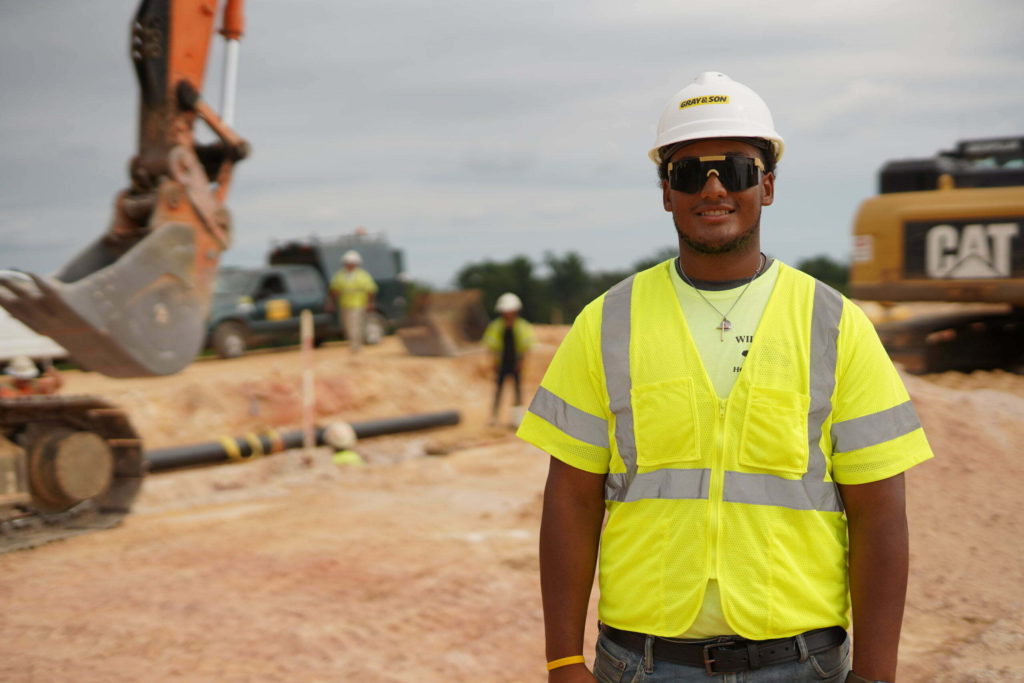 A male construction worker on construction site smiling for the camera working for company named Gray & Son a leading site and development contractor in Maryland.