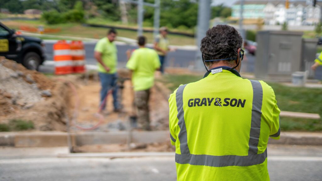 A male construction worker wearing a bright yellow vest with the company name " Gray & Son", Gray & Son is a leading site and development contractor in Maryland.