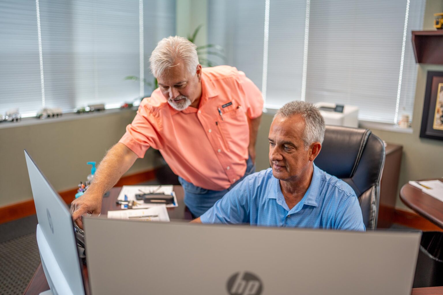 Two male workers who are working together in an office at two computers and work for Gray & Son a leading site and development contractor in Maryland.