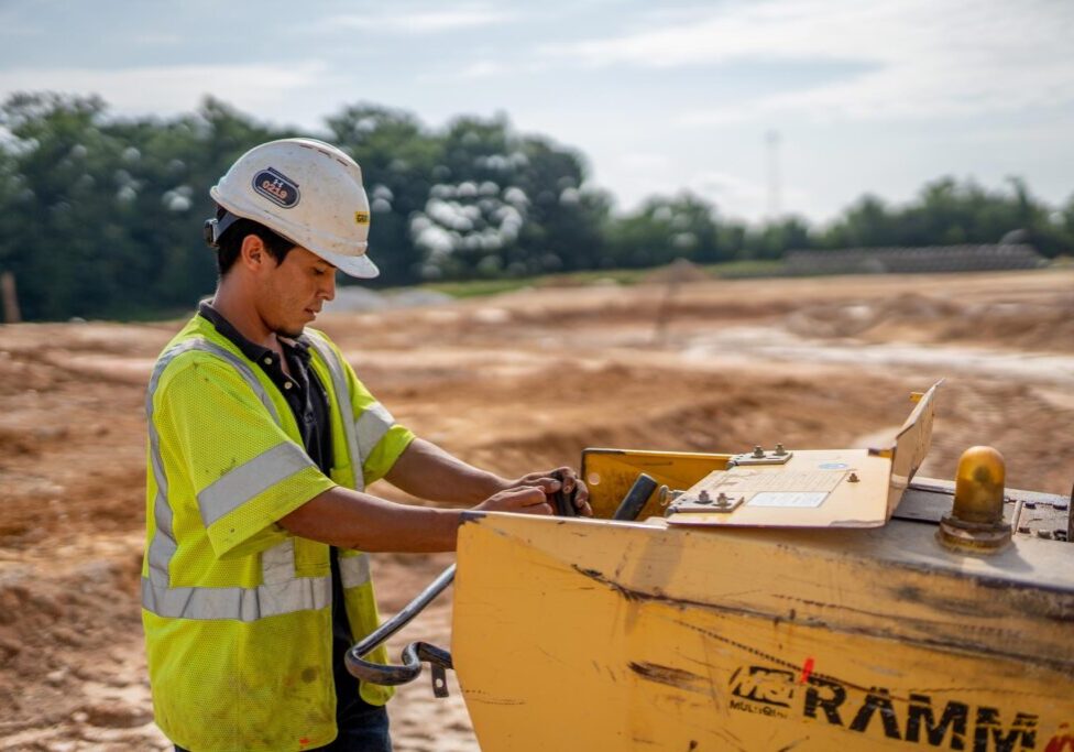 a male construction worker, in a dirt field controlling a machine who works for Gray & Son a leading site and development contractor in Maryland.