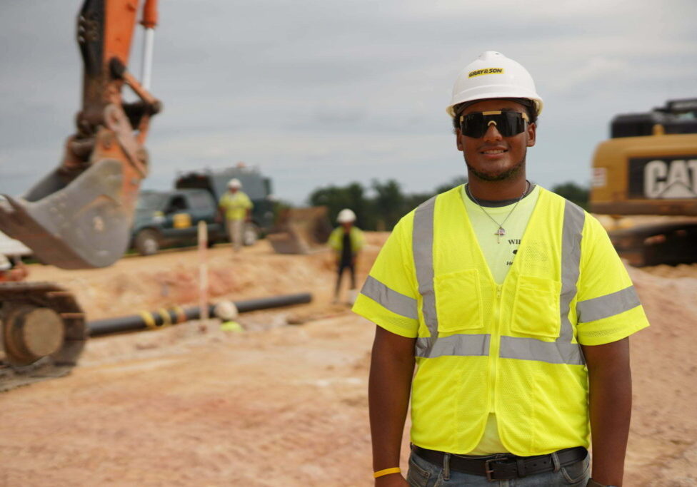A male construction worker on construction site smiling for the camera working for company named Gray & Son a leading site and development contractor in Maryland.