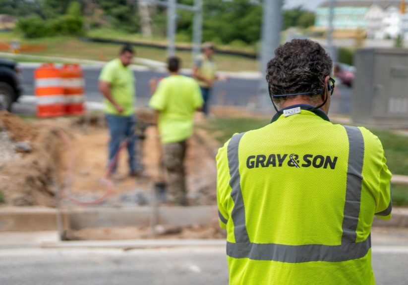 A male construction worker wearing a bright yellow vest with the company name " Gray & Son", Gray & Son is a leading site and development contractor in Maryland.